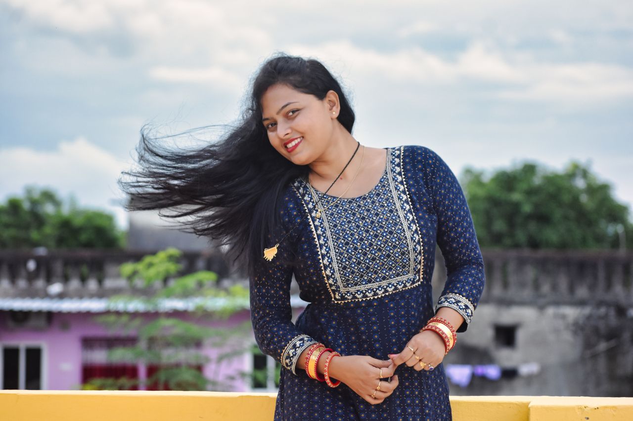 A smiling South Asian woman in a blue dress posing outdoors in Bhubaneswar, India.