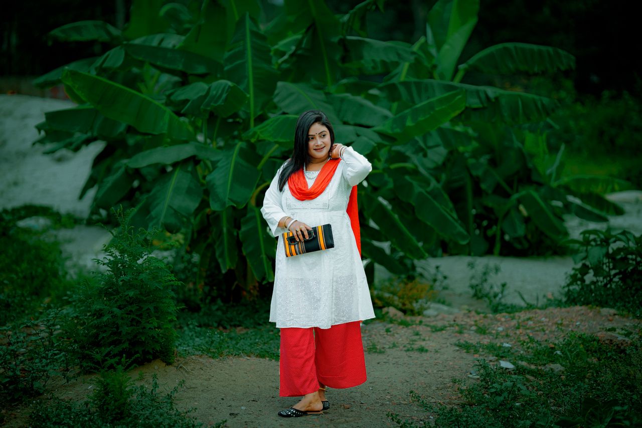 Woman poses outdoors with lush banana plants in traditional attire.