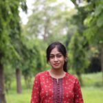 The Art of Drawing Readers In: Your attractive post title goes here Portrait of a young woman in a red kurti standing outdoors with lush greenery.