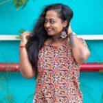 Mastering the First Impression: Your intriguing post title goes here Joyful woman in floral dress standing outside against blue wall, smiling confidently.