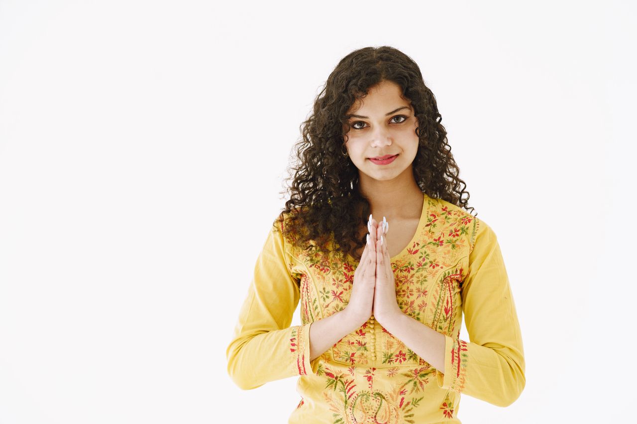 Portrait of a young woman in a yellow embroidered dress performing a traditional greeting with hands together.